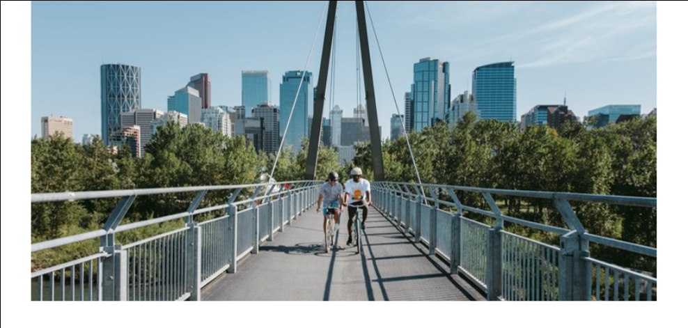 Cyclists crossing a bridge toward the Calgary skyline.